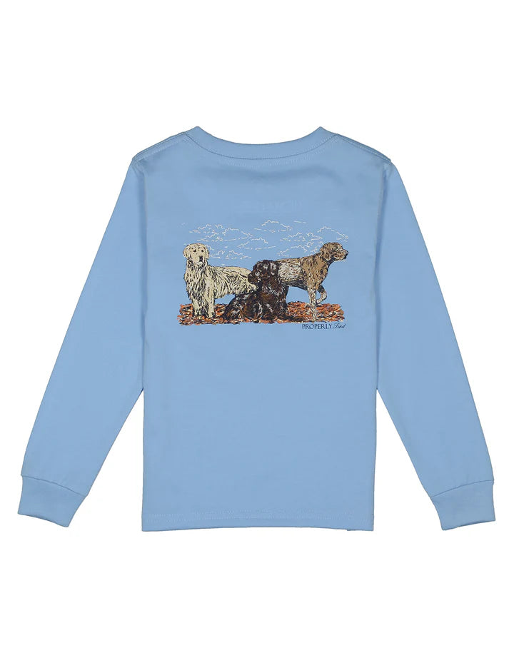 A light blue long-sleeve t-shirt shown from the back, featuring a graphic print of three dogs (a white dog, a black dog, and a brown dog) standing on a rocky outcrop under a cloudy sky.